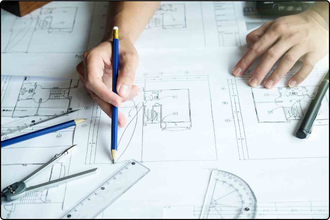 An architect’s hand holding a pencil, sketching detailed architectural plans on paper.